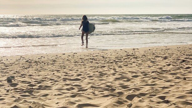 Ein Strand mit einer Person, die mit einem Surfbrett auf das Wasser zugeht.