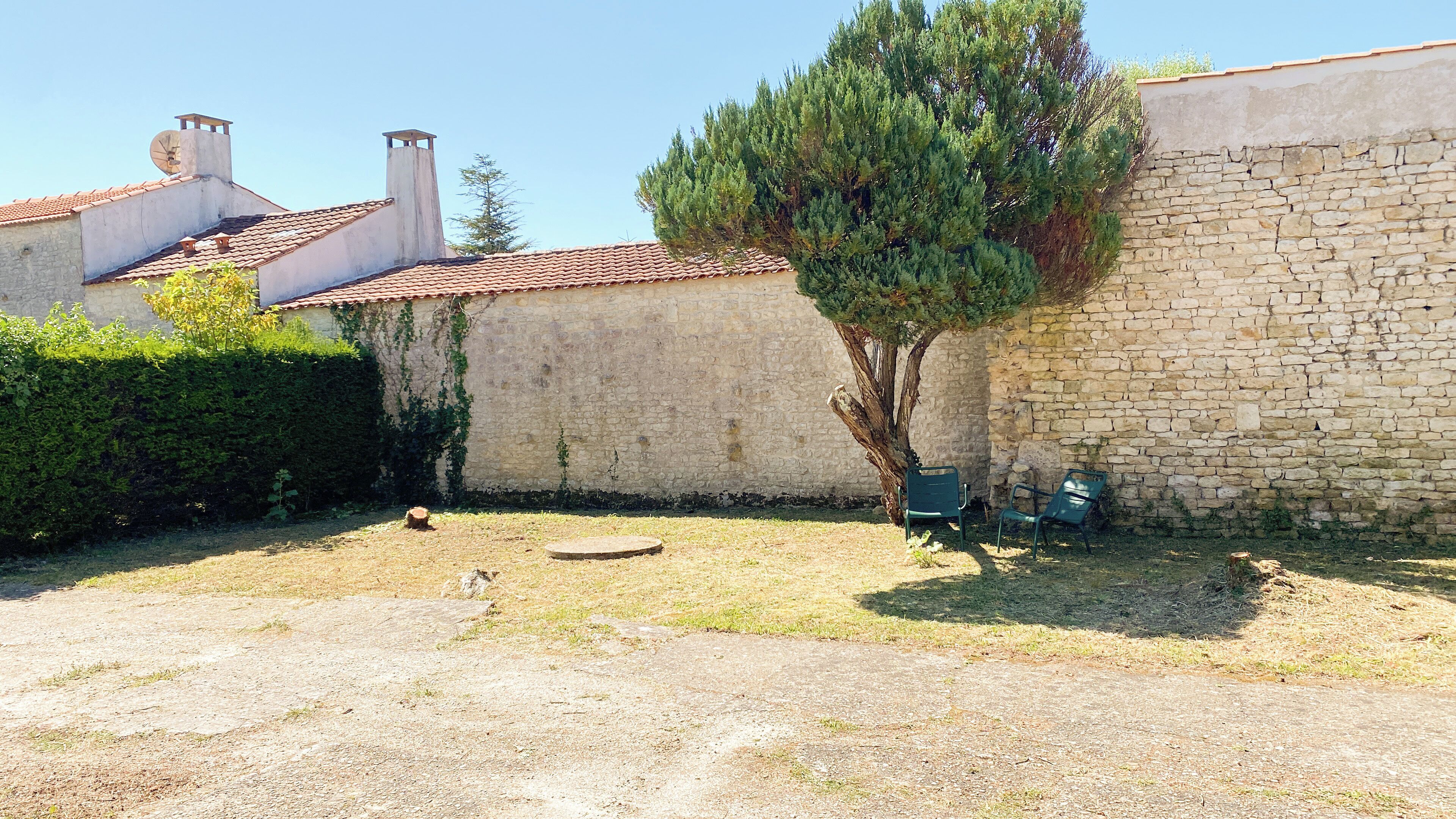 Un patio con muros de piedra, un árbol y una pequeña mesa redonda.