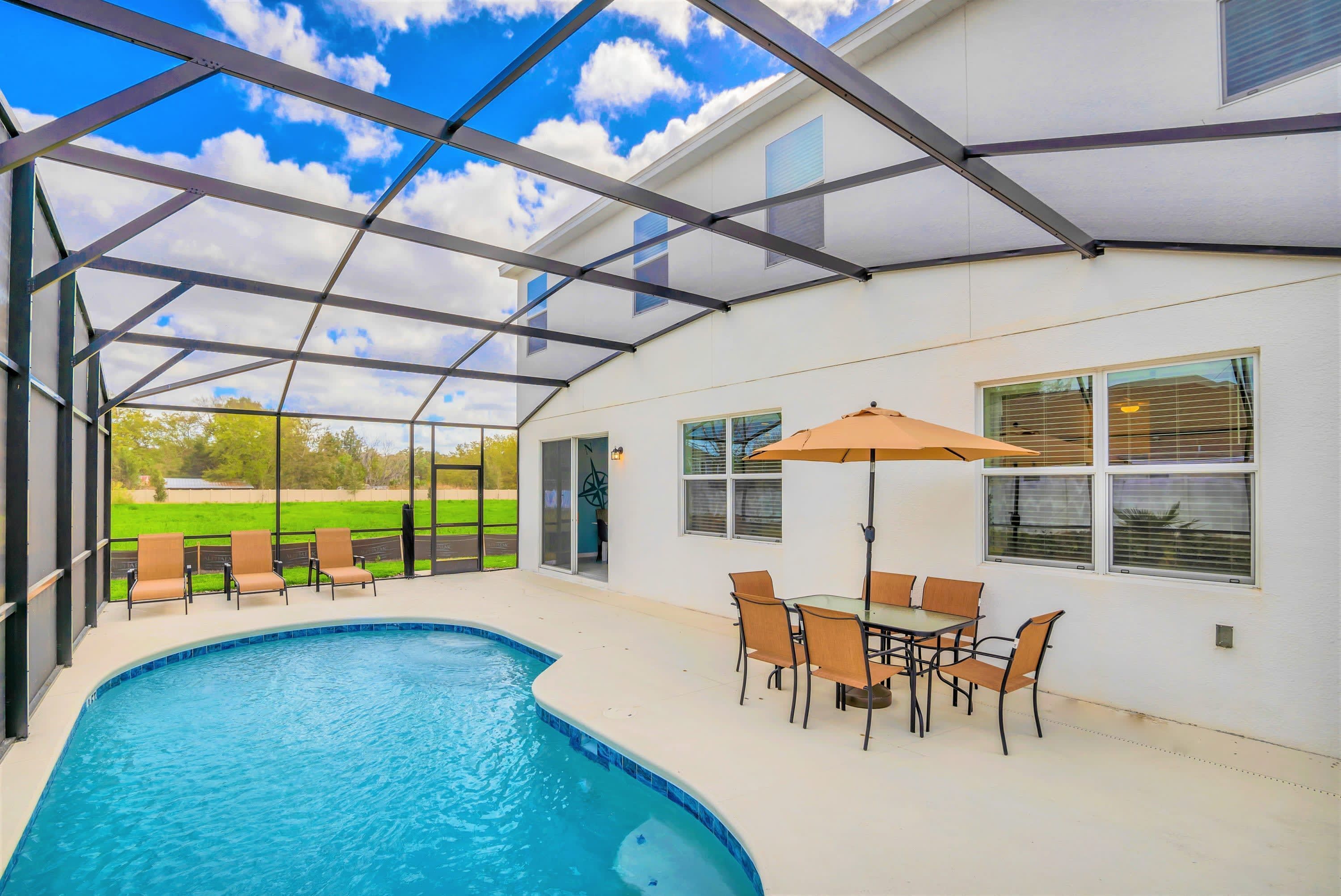 A covered outdoor swimming pool with a glass ceiling, a table with chairs, and a patio umbrella.