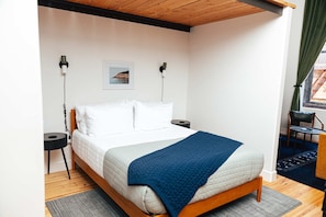Ein Schlafzimmer mit einem Bett, Nachttischen, einem Wandbild und einem Fenster mit Vorhängen.