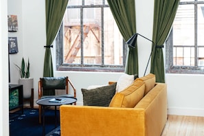 Ein Wohnzimmer mit einem gelben Sofa, einem kleinen runden Tisch, einem grünen Sessel und einer Stehlampe.
