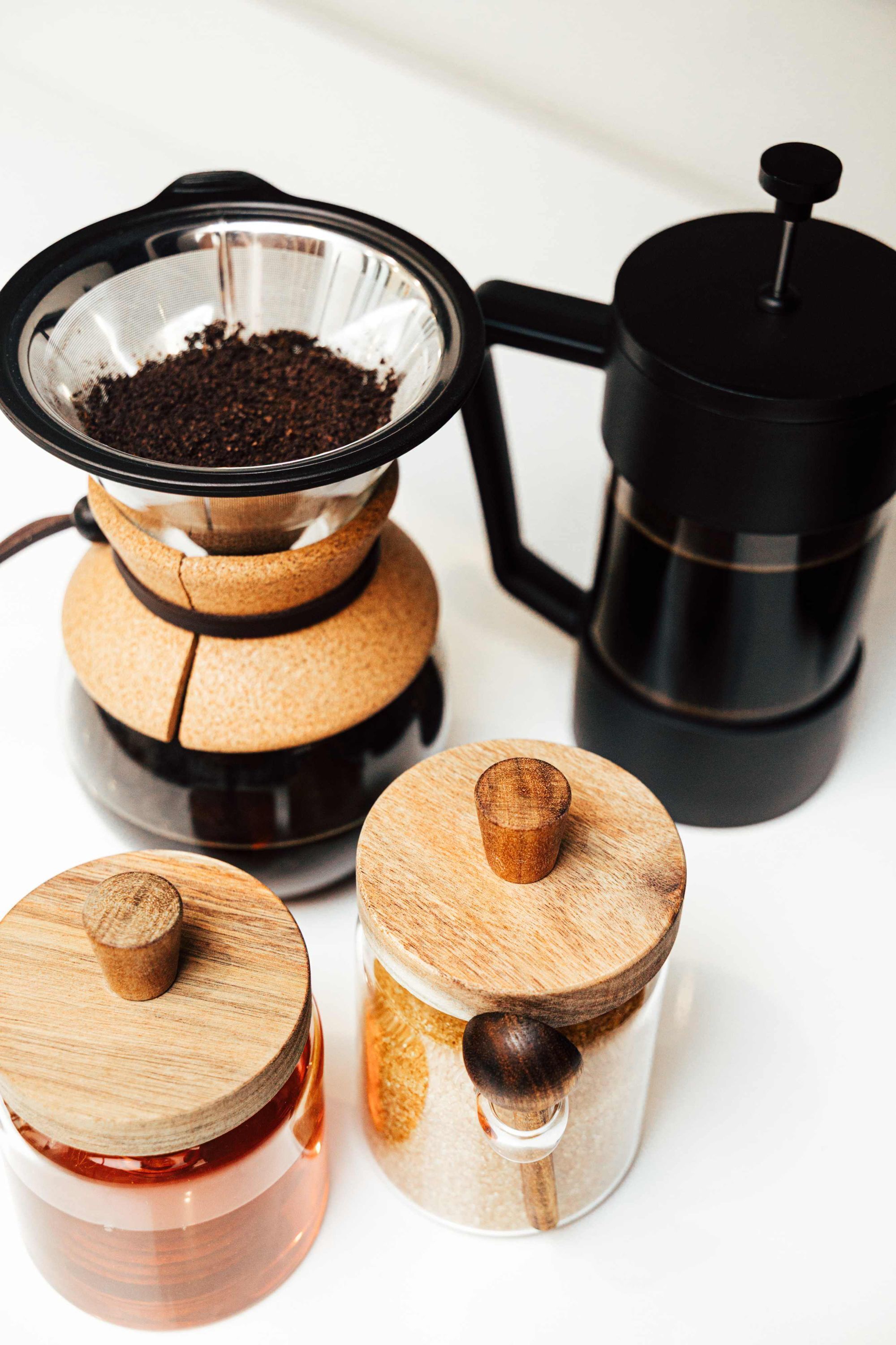 A coffee maker, a coffee pot, and two jars with wooden lids.