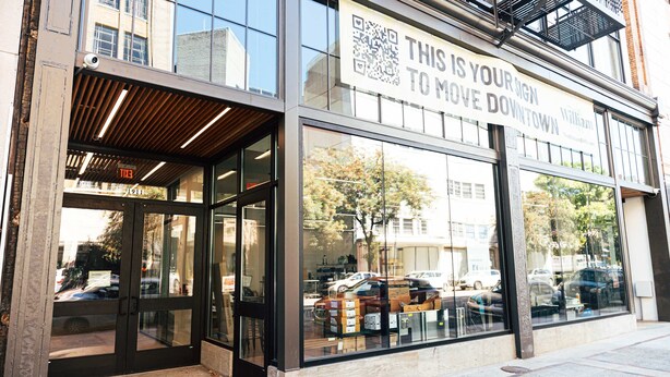 En bygning med store glasvinduer, et skilt der siger 'THIS IS YOUR SIGN TO MOVE DOWNTOWN', og en synlig brandstige.