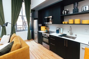 Une cuisine compacte dotée d’appareils électroménagers modernes, un coin repas avec un canapé jaune et une fenêtre avec des rideaux.