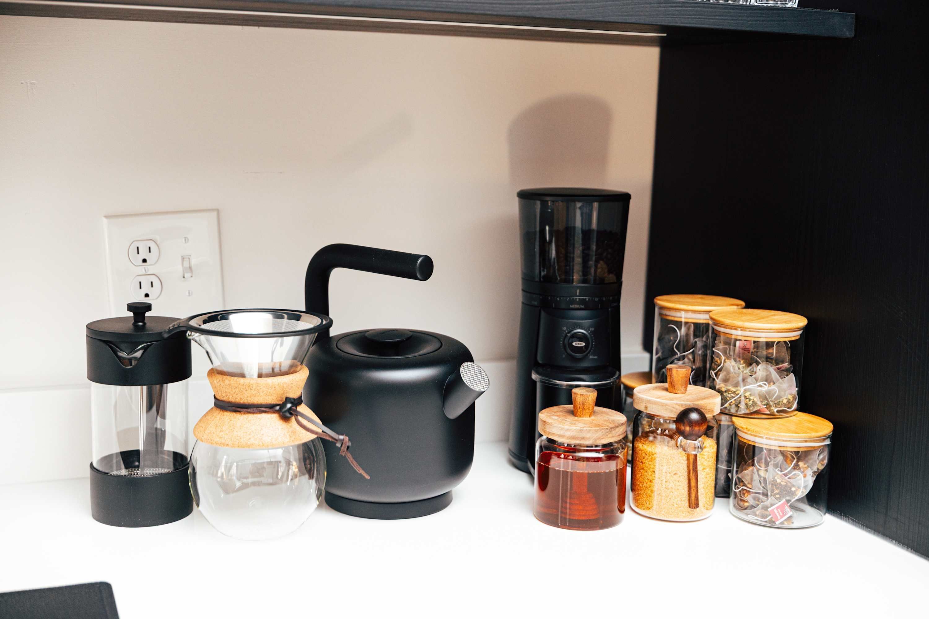 A kitchen with a coffee maker, a kettle, and several jars with lids.