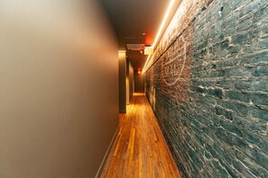 A hallway with wooden flooring, a brick wall on one side, and a light fixture on the ceiling.