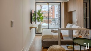 A modern bedroom with a large window, a bed, a bedside table, a green chair, and a potted plant. - NOK Modern 1BR Near Usaquen Unicentro (Bogotá)