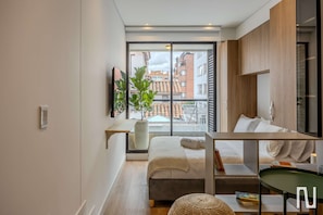 Ein modernes Schlafzimmer mit großem Fenster, einem Bett, einem Nachttisch, einem grünen Sessel und einem Topfpflanzen.