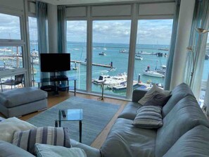 A living room with a large window, a flat-screen TV, a sofa, and a coffee table. - Spinnaker Apartment 3 bed Waterside Apartment (Cowes)