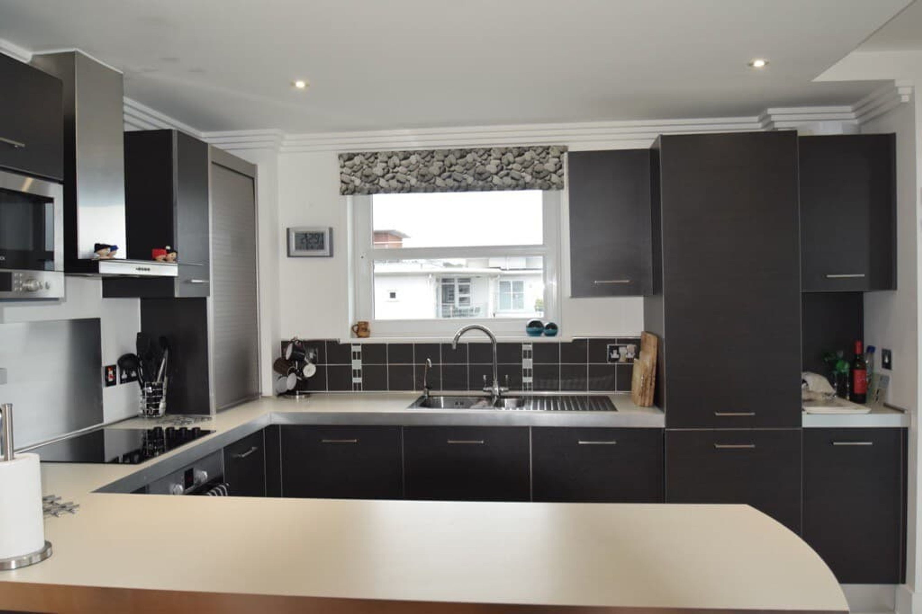A modern kitchen with dark cabinetry, a stainless steel range hood, and a window with a view of buildings outside.