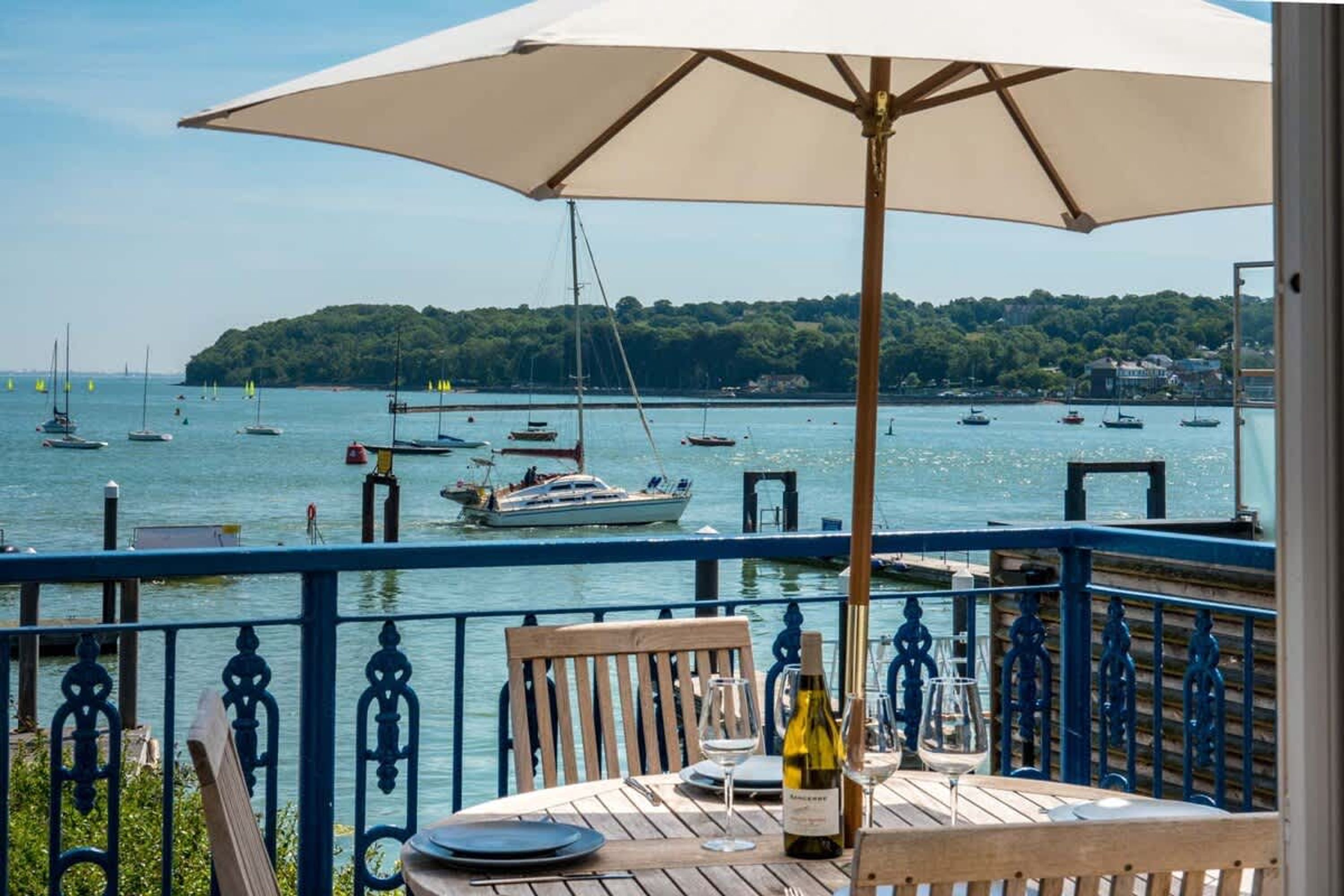 Una mesa con una botella de vino, una copa y una silla en un balcón con vista a un puerto deportivo y barcos.