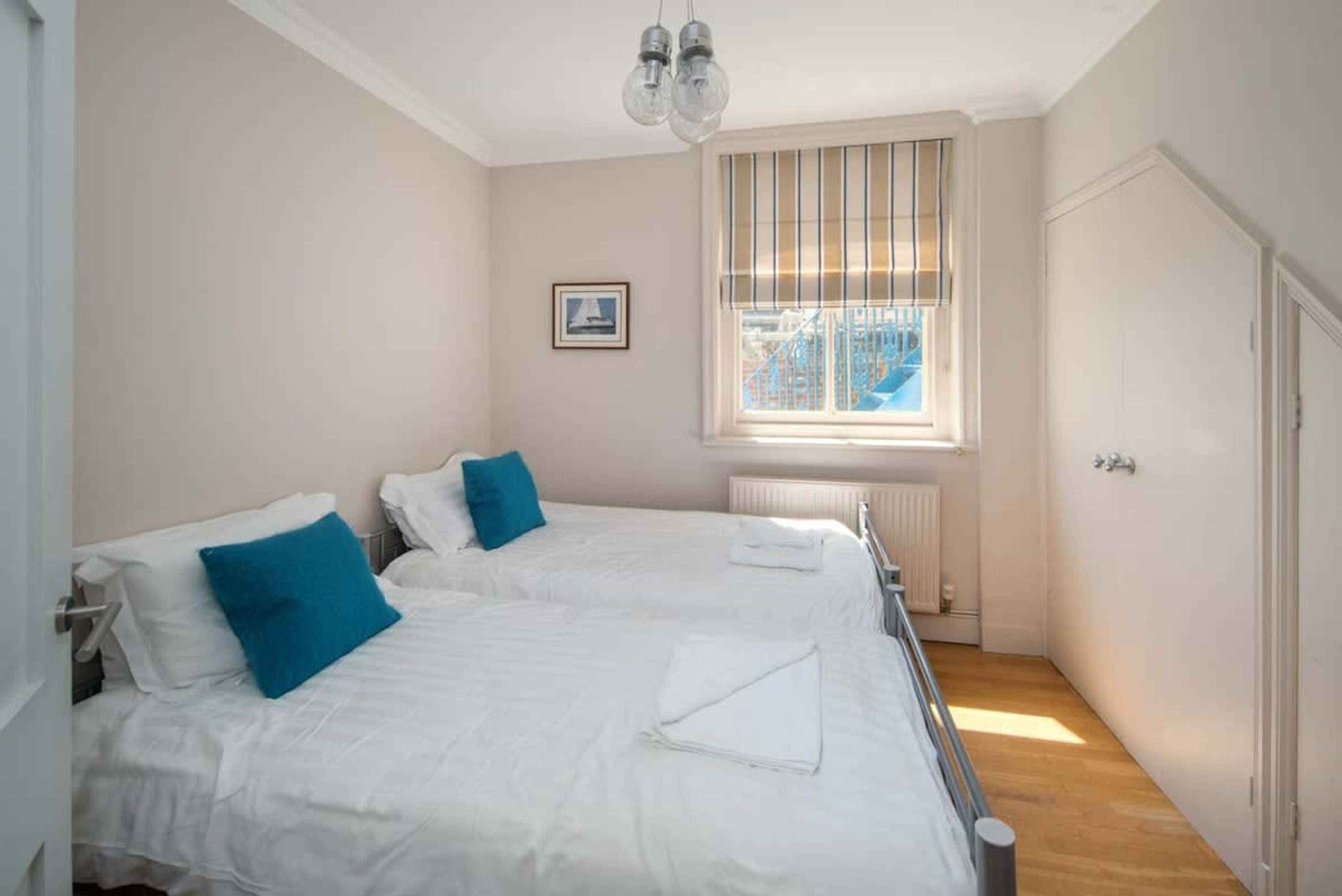 Une chambre avec deux lits, une fenêtre avec des stores, un radiateur et une porte.