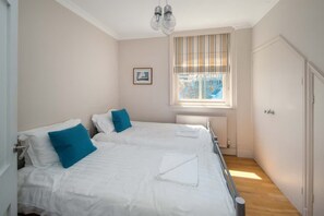 Ein Schlafzimmer mit zwei Betten, einem Fenster mit Jalousien, einem Heizkörper und einer Tür.