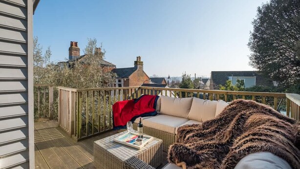 A wooden deck with a wicker sofa, a red blanket, and a glass of wine on a table. - Park View 5 Bedroom Home With Solent Park Views (Cowes)