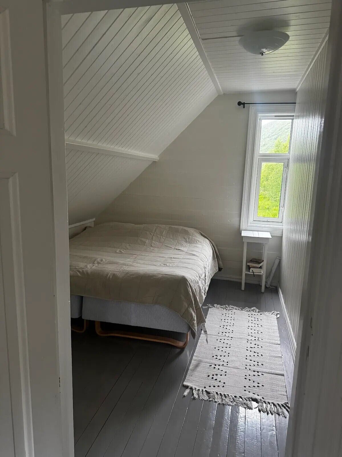 Un dormitorio con una cama, una mesita, un ventanal y un ventilador de techo.
