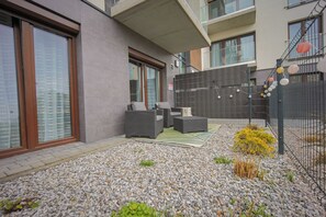 Um pátio externo moderno com área de estar, piso de cascalho e cerca.