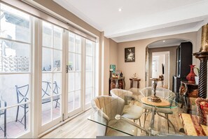 Un vaste espace de vie comprenant une table à manger en verre, des sièges confortables et de grandes fenêtres offrant une vue sur l’extérieur.