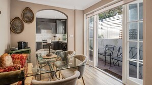 Un salón moderno con una mesa de centro de vidrio, asientos cómodos, una cocina al fondo y un ventanal corredero que da a un espacio exterior.