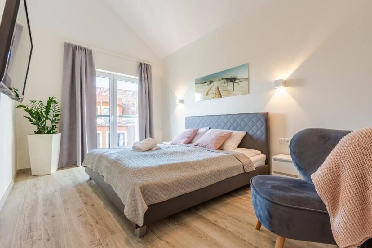 Un dormitorio con cama, una silla, una planta en maceta y un cuadro en la pared.