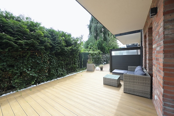 A wooden deck with outdoor furniture, a brick wall, and a hedge.