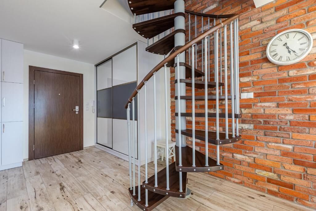 Eine Wendeltreppe mit Metallgeländern, Holzverkleidung und einer Backsteinwand mit einer Uhr.