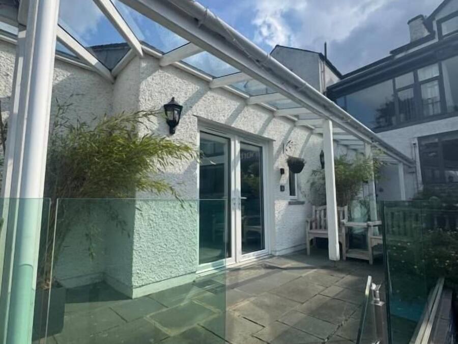 A covered outdoor area with a glass roof, stone flooring, and a white wall with a window.