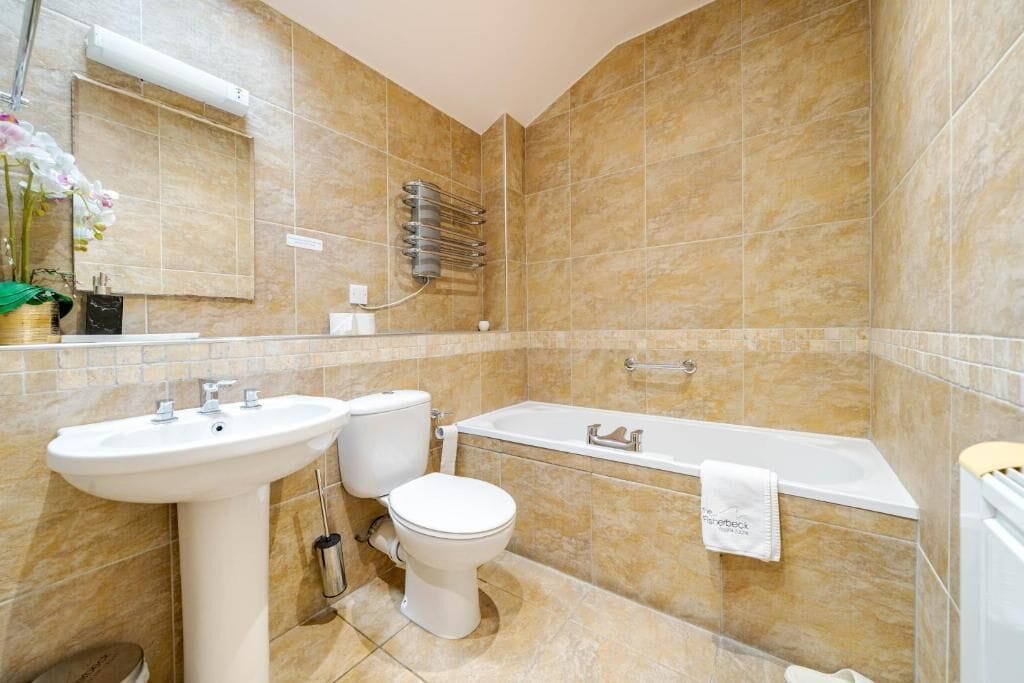 Une salle de bain équipée d’un lavabo, de toilettes et d’une baignoire, avec une serviette suspendue à la baignoire.