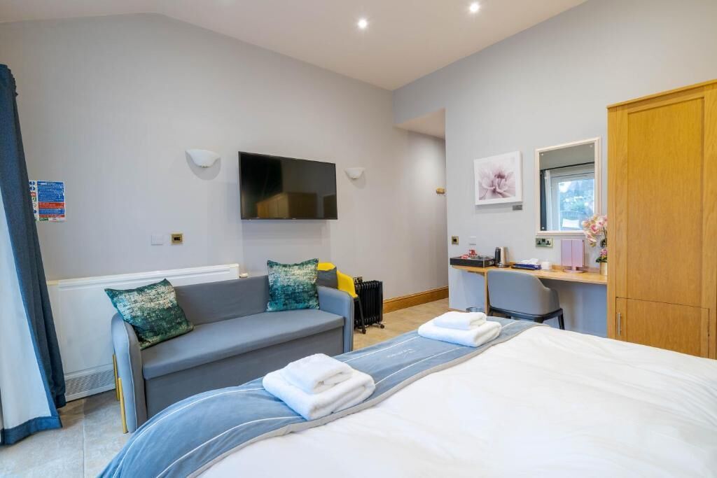 Habitación de hotel con cama, sofá, escritorio, televisor y armario de madera.