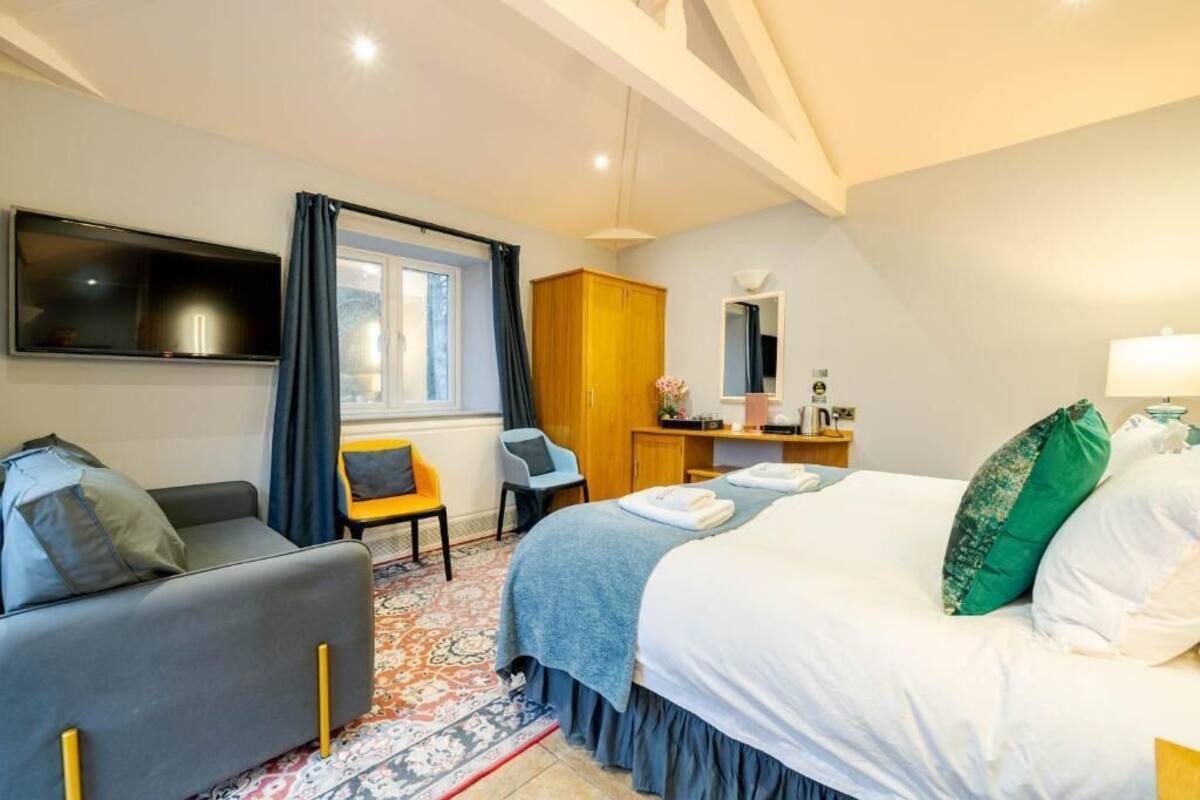 A hotel room with a bed, a sofa, a desk with a mirror, and a television on the wall.