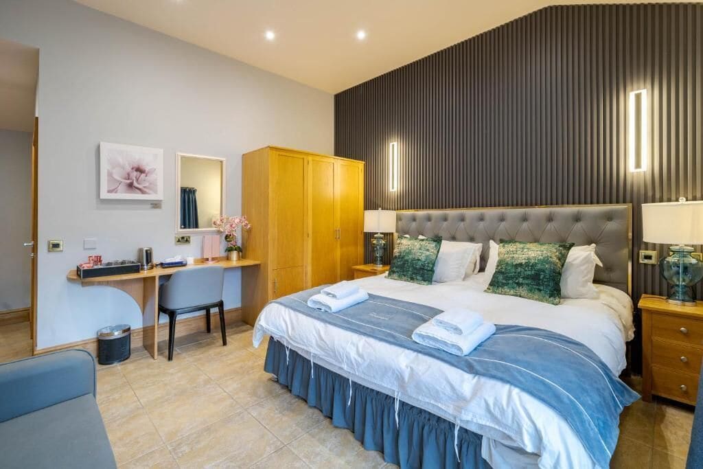 A modern bedroom with a large bed, a desk, a wardrobe, and a bedside table.