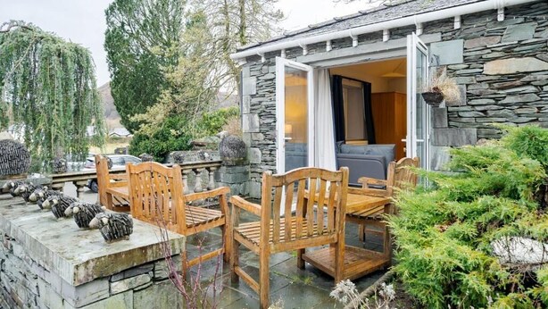 A stone building with a patio area featuring wooden furniture and a stone wall. - Waterhead Retreat (Ambleside)