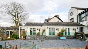 A waterfront property with a stone patio, wooden bridge, and a row of windows. - Waterhead Retreat (Ambleside)