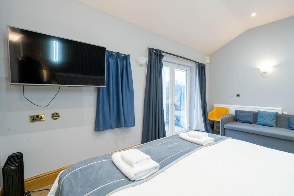 Una habitación de hotel con cama, televisión, ventana con cortinas, sofá y lámpara.