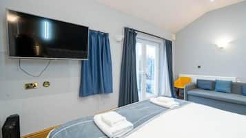 Una habitación de hotel con cama, televisión, ventana con cortinas, sofá y lámpara.