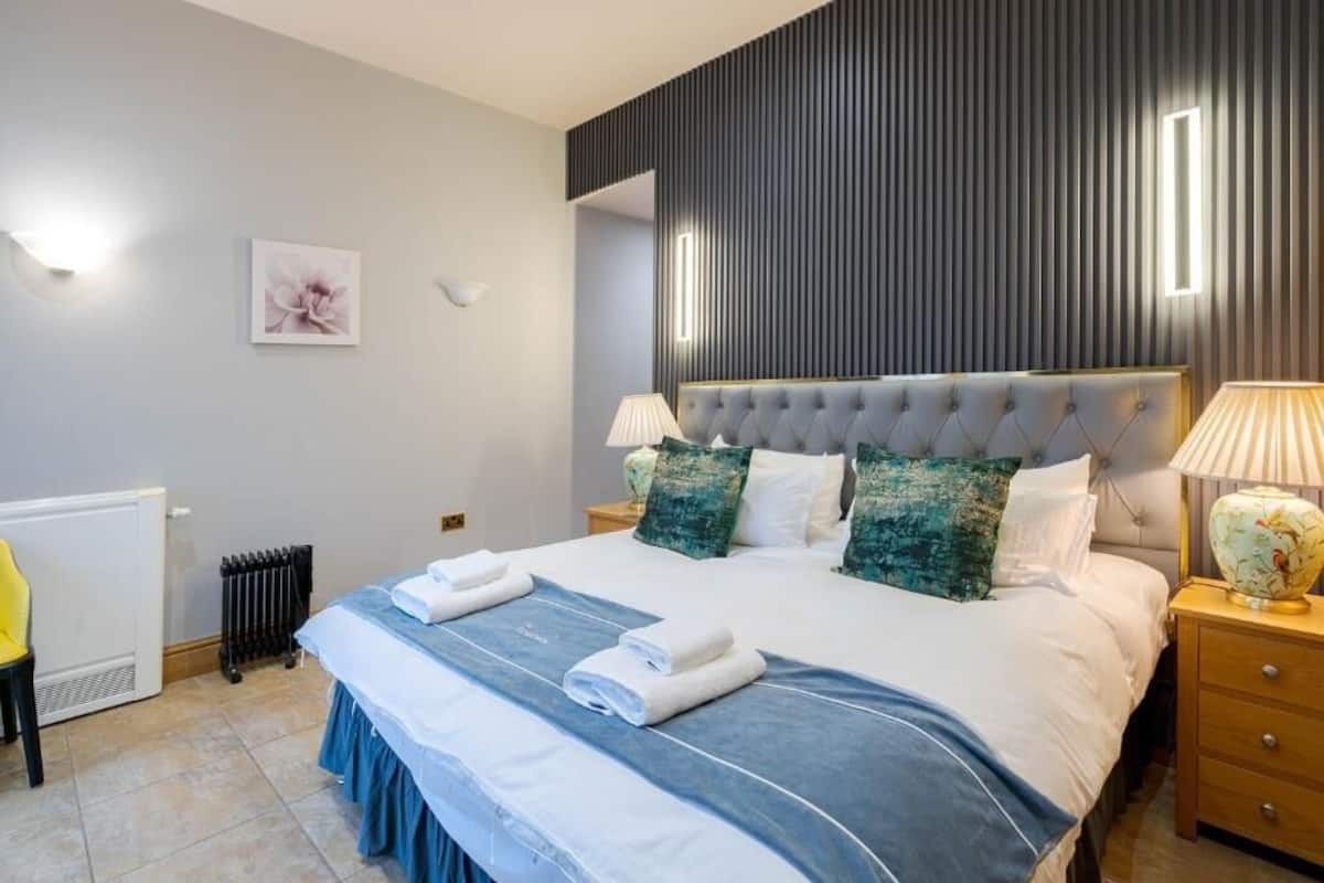 A neatly made bed with pillows, a bedside lamp, and a radiator.