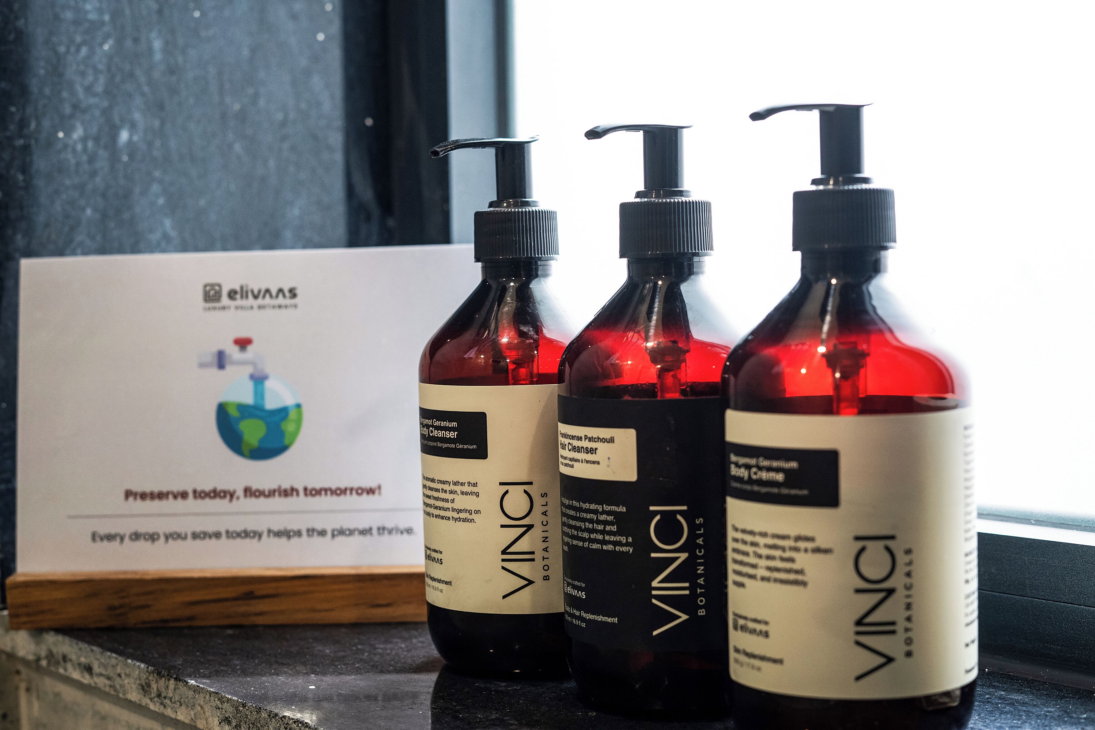 Tres botellas de productos corporales VINGI Botanical sobre una encimera con un cartel sobre la protección del medio ambiente.