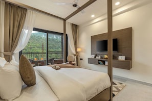 A hotel room with a bed, curtains, a TV, a balcony with a view, and a desk with a chair. - ELIVAAS Panchvati Veloraa 3BHK (Solan)