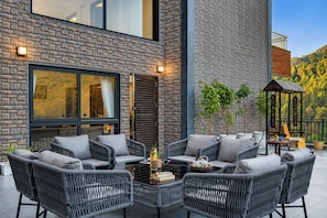 A modern outdoor seating area with wicker furniture, a glass table, and potted plants.