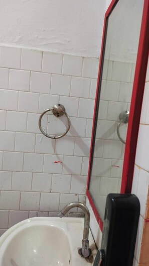 A bathroom with white tiled walls, a sink, a mirror with a red frame, and a towel ring.