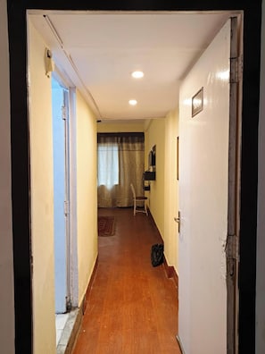 Un pasillo estrecho con suelo de madera, una puerta a la derecha y una silla al fondo.