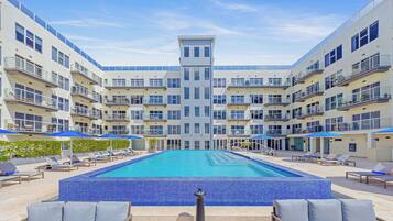 Ein modernes Hotel mit einem zentral gelegenen Schwimmbad, umgeben von Liegebereichen und mehreren Balkonen.