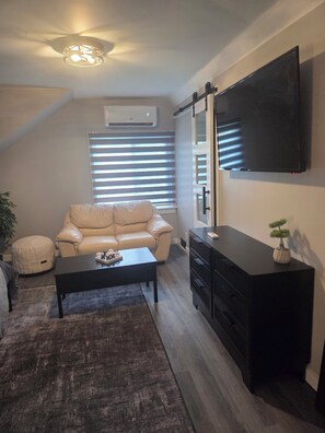 Una sala de estar con un sofá, una mesa de centro, un televisor, un aparador y una planta en maceta.