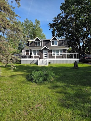 A two-story house with a front porch, a small front yard, and a large tree to the right.