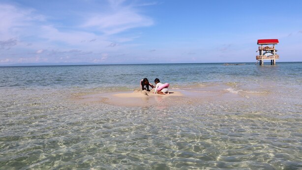 A beach with clear water, a lifeguard tower, and two people playing in the sand. - Mi Corazón Resort (Mabini)
