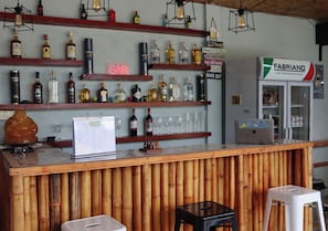 A bar area with shelves of liquor bottles, a neon sign, a laptop, and a refrigerator.