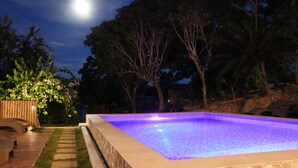 A swimming pool with a tiled edge, surrounded by trees and a wooden deck. - Mi Corazón Resort (Mabini)