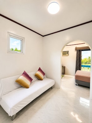 A bedroom with a bed, a window, and an arched doorway leading to another room. - Mi Corazón Resort (Mabini)