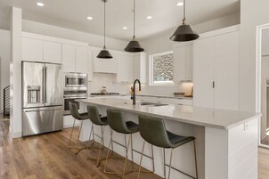 Una cocina moderna con una isla central, electrodomésticos de acero inoxidable y taburetes de bar.