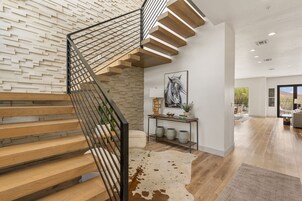 Una escalera moderna con escalones de madera y barandilla metálica, un estante empotrado con objetos decorativos, y un ventanal grande al fondo.