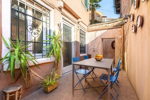 Eine Terrasse mit Tisch, Stühlen, Blumentöpfen und einem Fenster mit schmiedeeisernen Verzierungen.